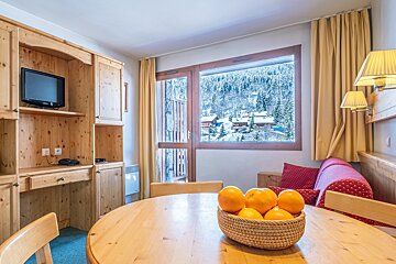 A bowl of oranges sits on a wooden table in a living room