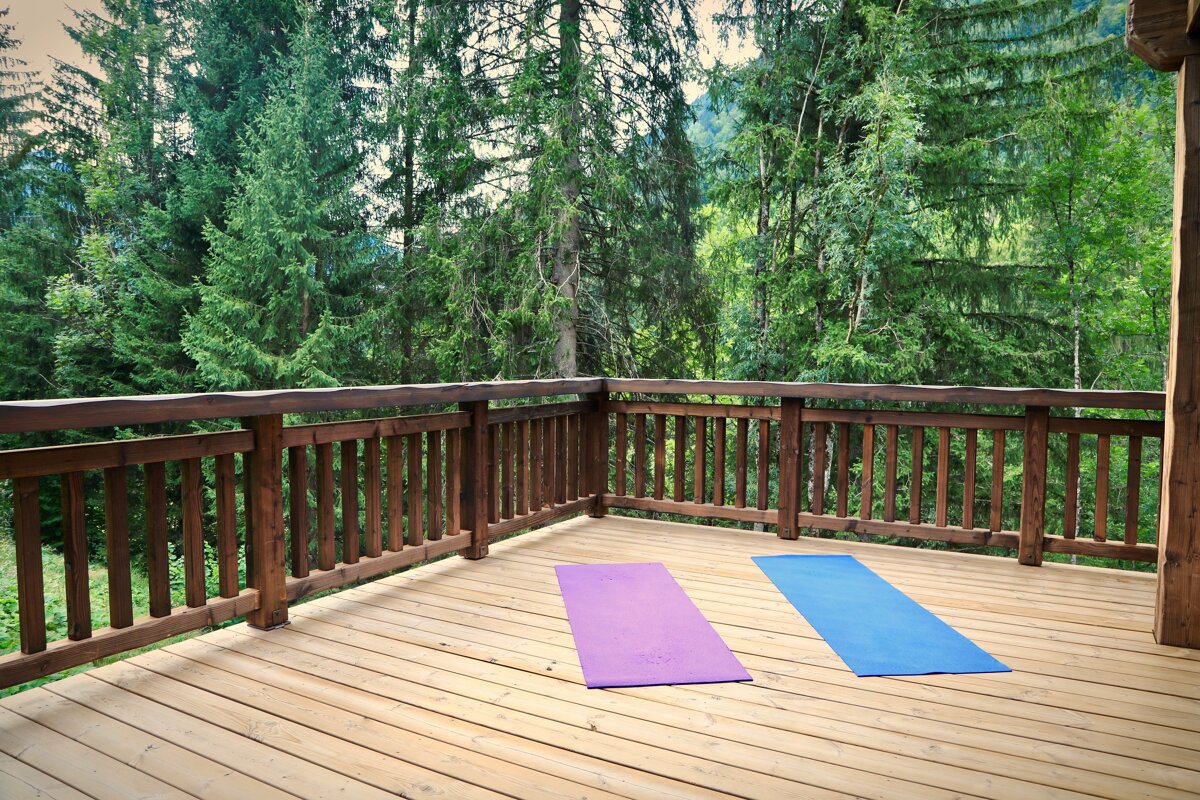 Two colorful yoga mats lie on a wooden deck, overlooking a dense, green forest.