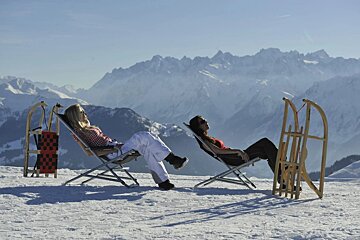 Two women sit in lawn chairs next to sleds in the snow