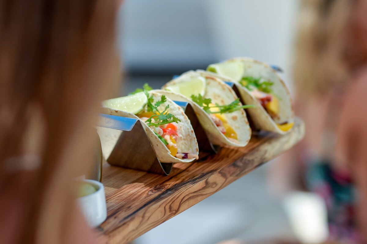 A row of tacos are lined up on a wooden tray