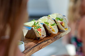 A row of tacos are lined up on a wooden tray