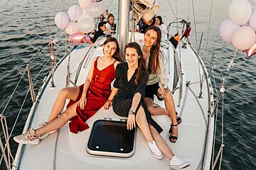 Three women are sitting on a sailboat with balloons and champagne