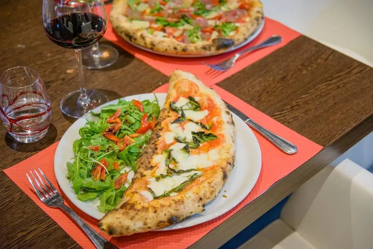 A half eaten pizza on a plate next to a glass of wine