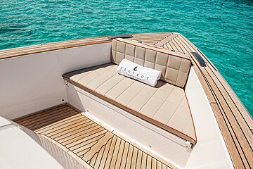 A luxury boat bow with a beige cushioned seat, a white towel, and teak decking overlooking clear turquoise water.