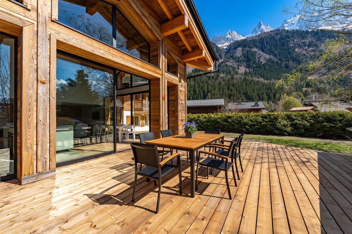 A wooden deck with a table and chairs and mountains in the background