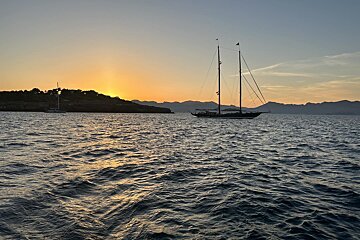 A sailboat in the middle of the ocean at sunset