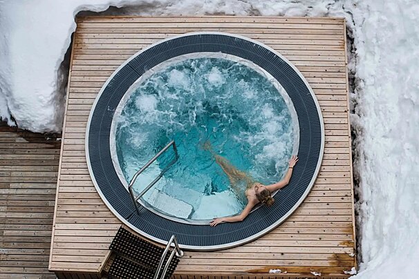 A woman is laying in a hot tub surrounded by snow