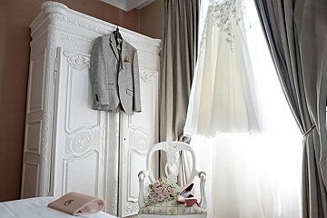 A wedding dress hangs on a white wardrobe next to a chair
