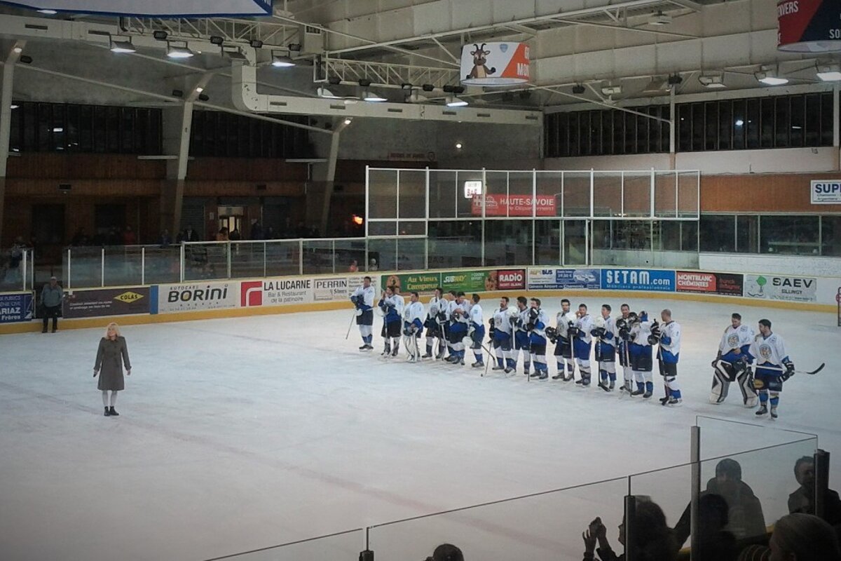 a girl in the centre of the ice rink & a team lined up in blue & white