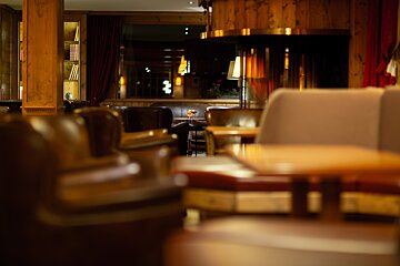 A dimly lit, cozy lounge with classic leather seating, wooden interiors, bookshelves, and cocktails, evoking a warm, inviting ambiance.