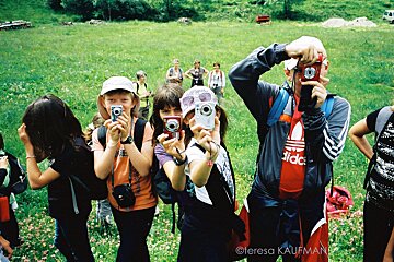 A man wearing an adidas shirt takes a picture of a group of people