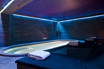 A luxurious spa room with a starry ceiling, blue LED lighting, a warm hot tub, and comfortable loungers with fresh towels.