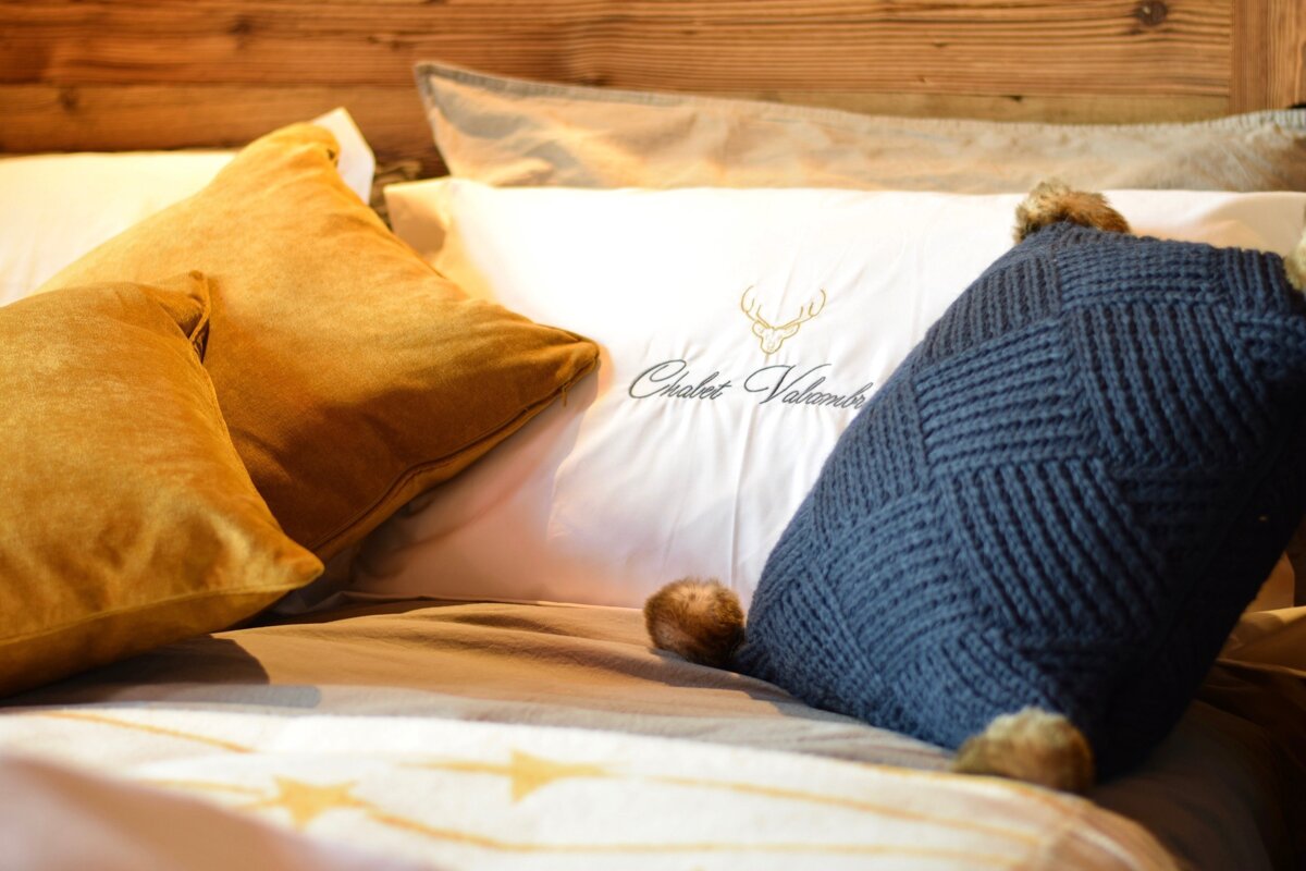 A cozy bed with a wooden headboard, adorned with gold velvet pillows, a white pillow with 