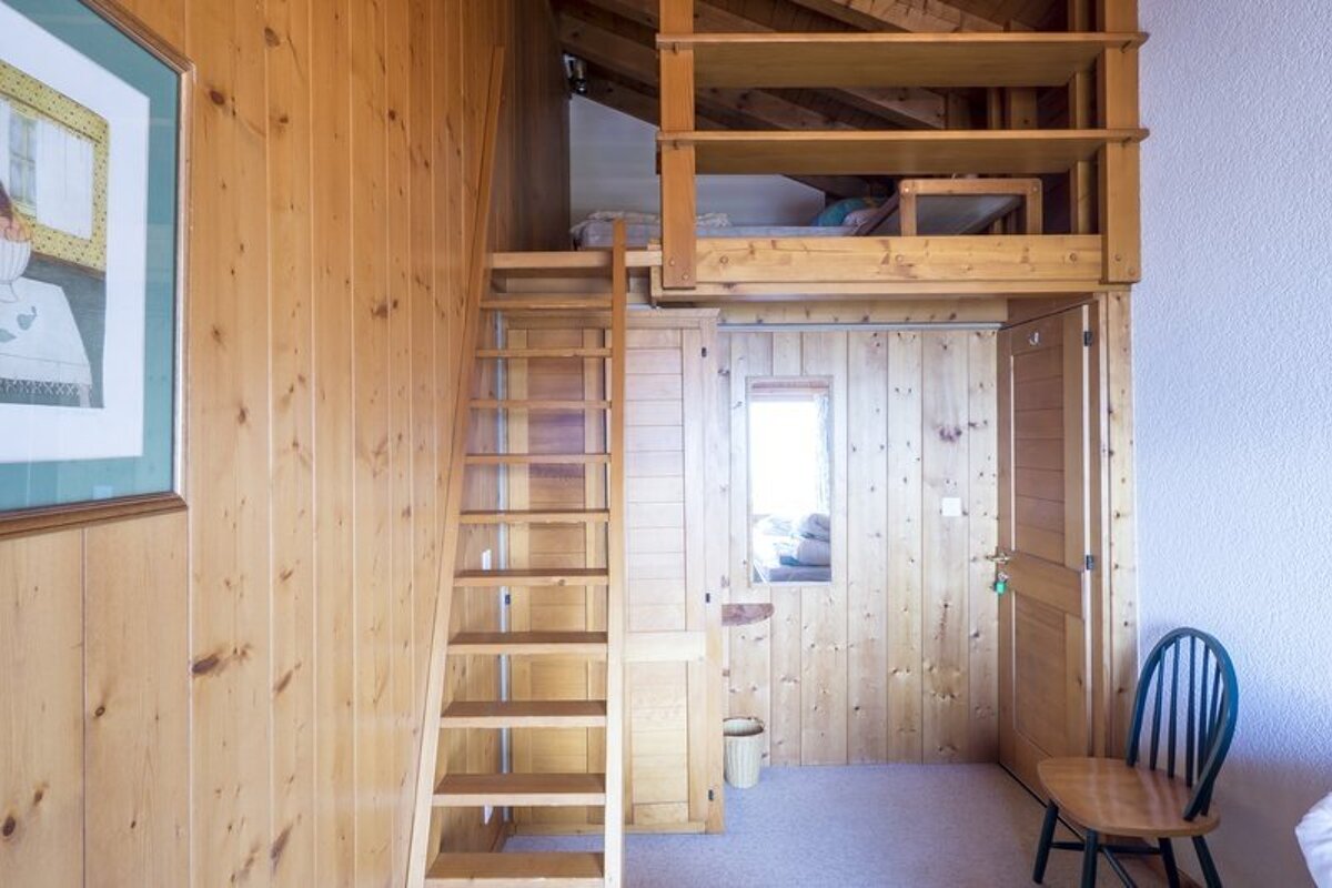 Cozy wooden cabin room featuring a ladder leading to a loft bed and paneled walls.
