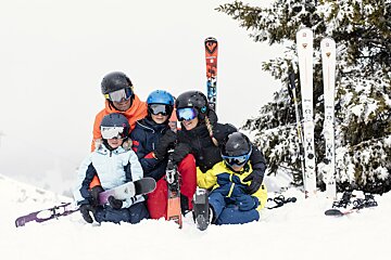 A family laying in the snow with skis and snowboards including one that says rossignol