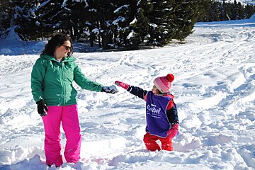 A woman and child are playing in the snow and the woman is wearing a purple shirt that says meribel