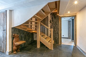 A wooden bear statue sits under a staircase in a hallway