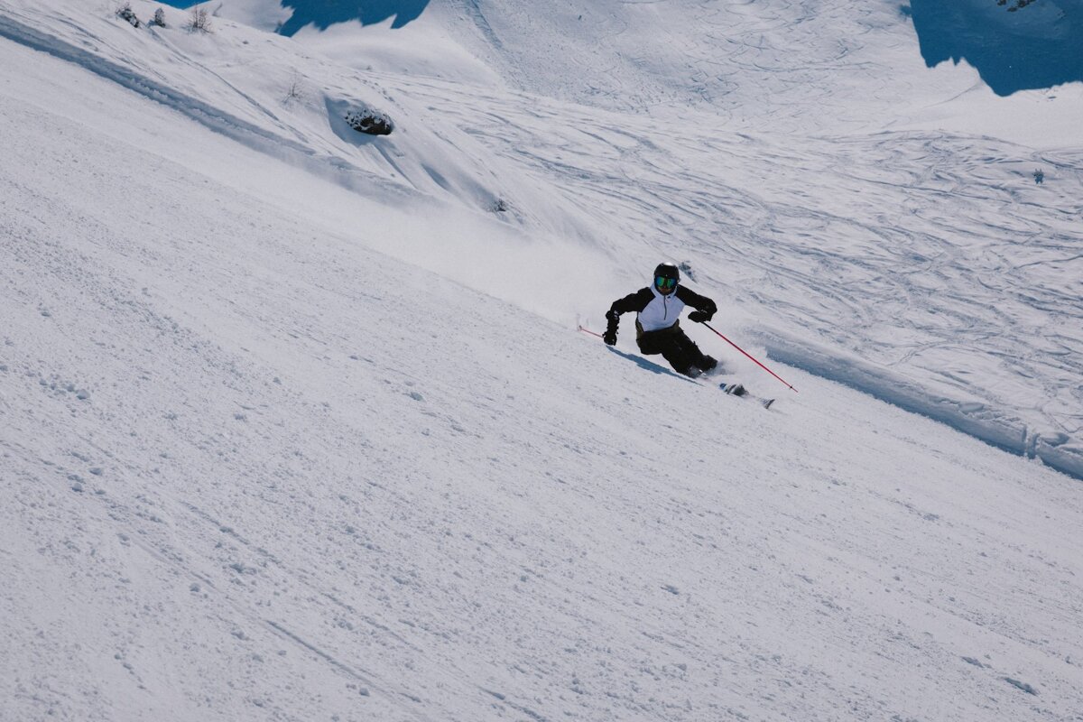 A person skiing down a snowy slope with a snowboarder in the background