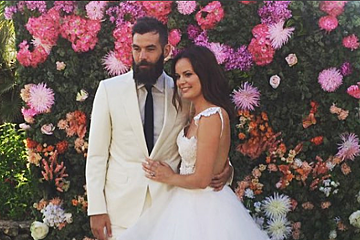 A bride and groom pose in front of a wall of flowers