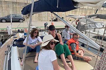 A group of people sitting on a boat with one wearing a life jacket