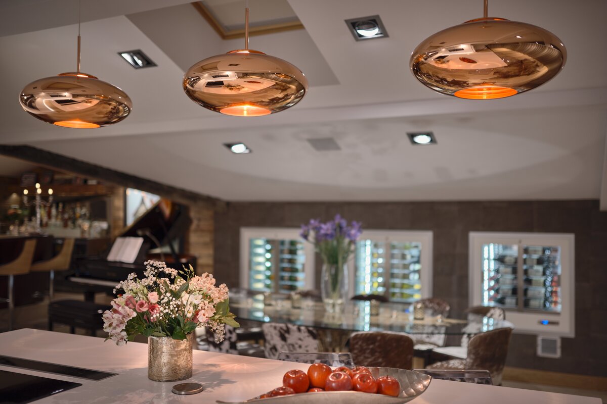 A bowl of tomatoes sits on a counter next to a vase of flowers