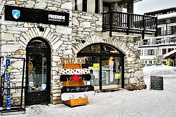 A snowy Freeride snowboard & ski shop in a stone building, displaying skis and snowboards outside on a winter day.