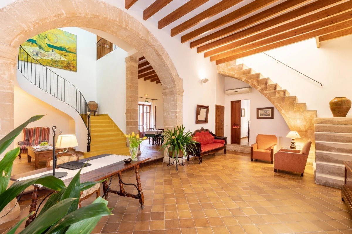 Spacious, traditional hall with stone arches, wooden beams, a yellow spiral staircase, a stone staircase, and inviting seating areas.