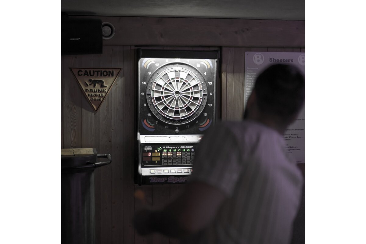 A blurred person throws darts at an electronic dartboard. A