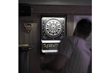 A blurred person throws darts at an electronic dartboard. A