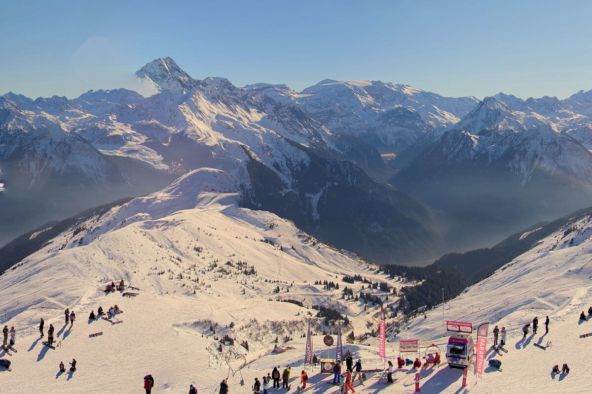 A vibrant ski resort scene on a sunny day, with skiers and snowboarders on snow-covered slopes surrounded by majestic mountains.