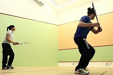 A man and a woman are playing tennis and the man is wearing asics pants