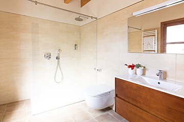 A modern, minimalist bathroom with beige tiles, a glass walk-in shower, wall-mounted toilet, and a sleek wooden vanity with a mirror.