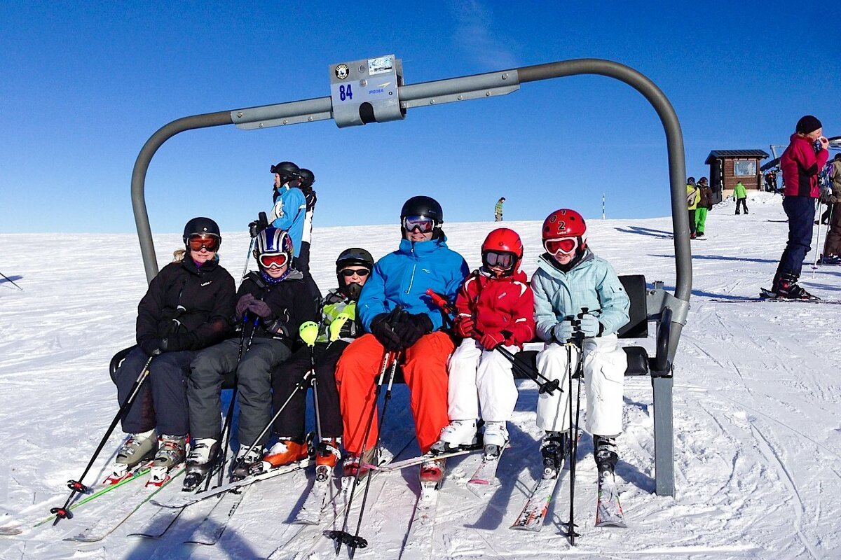 A group of skiers are sitting on a ski lift with the number 84 above them