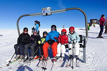 A group of skiers are sitting on a ski lift with the number 84 above them