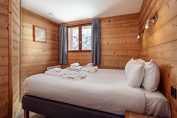 A bedroom with wooden walls and a bed with white sheets