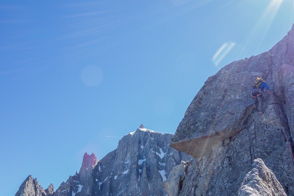 A person climbs a mountain with a blue sky in the background