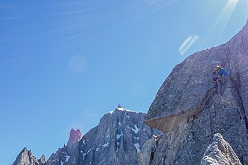 A person climbs a mountain with a blue sky in the background