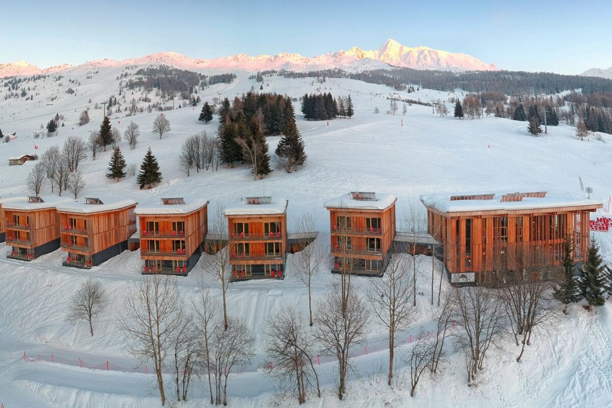 A row of wooden buildings in the snow with mountains in the background