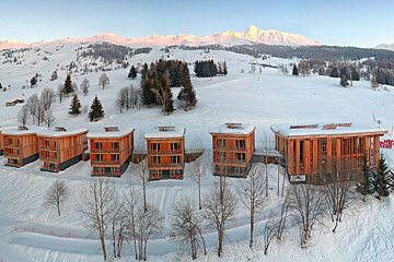 A row of wooden buildings in the snow with mountains in the background