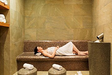 A woman wrapped in a towel is laying on a bench