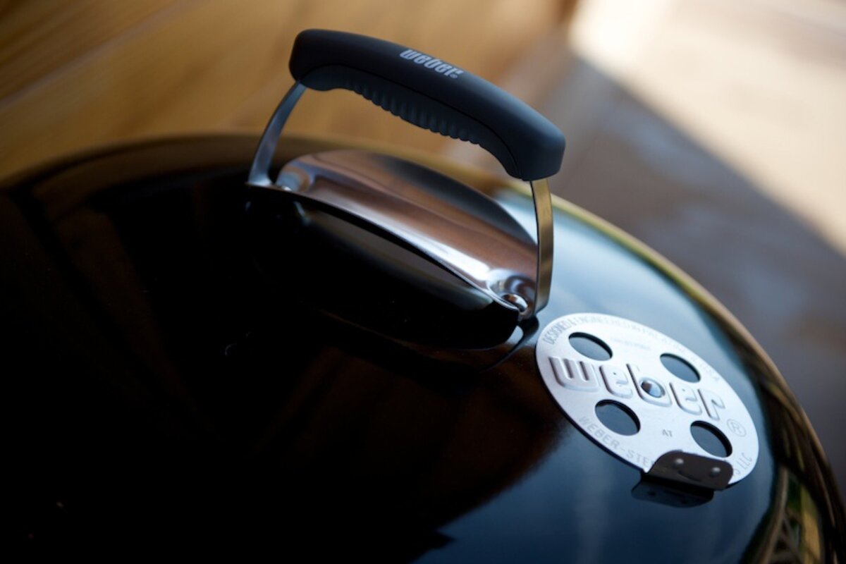 Close-up of a black Weber grill lid, showing its handle and the iconic Weber logo on the round vent.