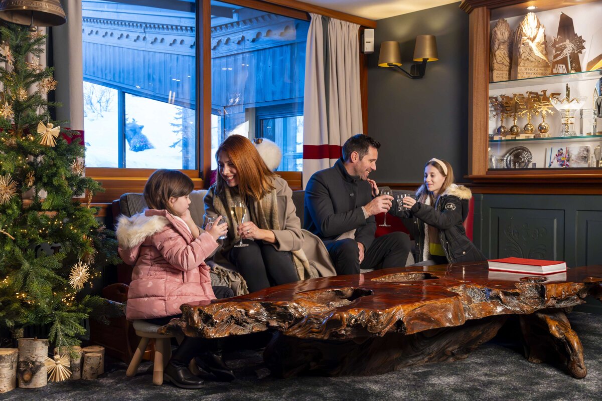 A family sits on a couch drinking champagne in front of a christmas tree