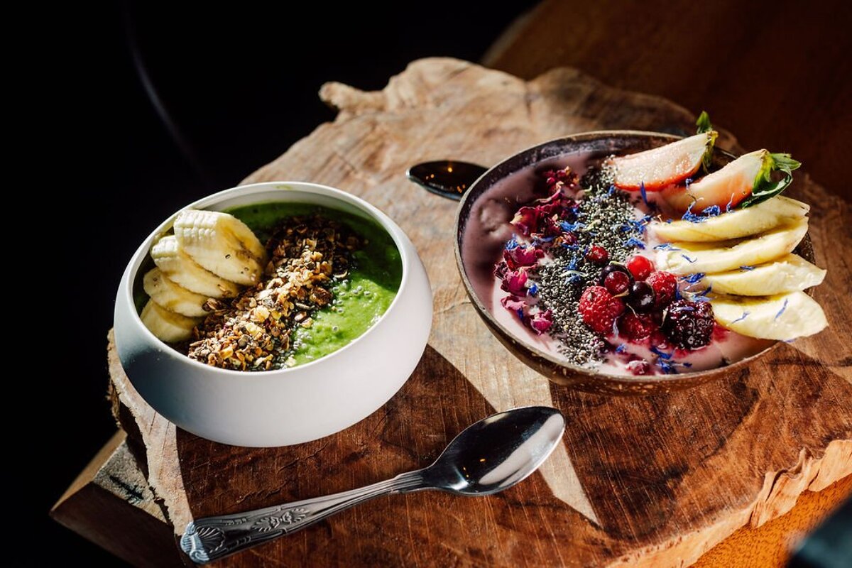 Two bowls of food on a wooden table with a spoon