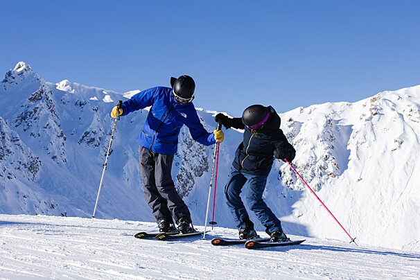 A man in a blue jacket helps a woman ski down a snowy slope