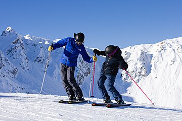 A man in a blue jacket helps a woman ski down a snowy slope