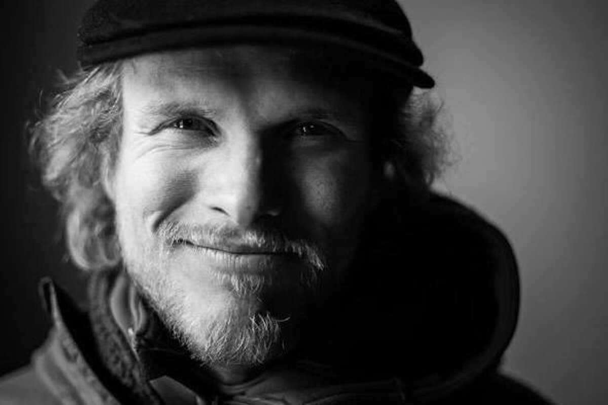 A black and white photo of a man with a beard wearing a hat and smiling