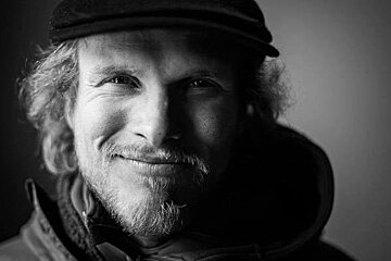 A black and white photo of a man with a beard wearing a hat and smiling