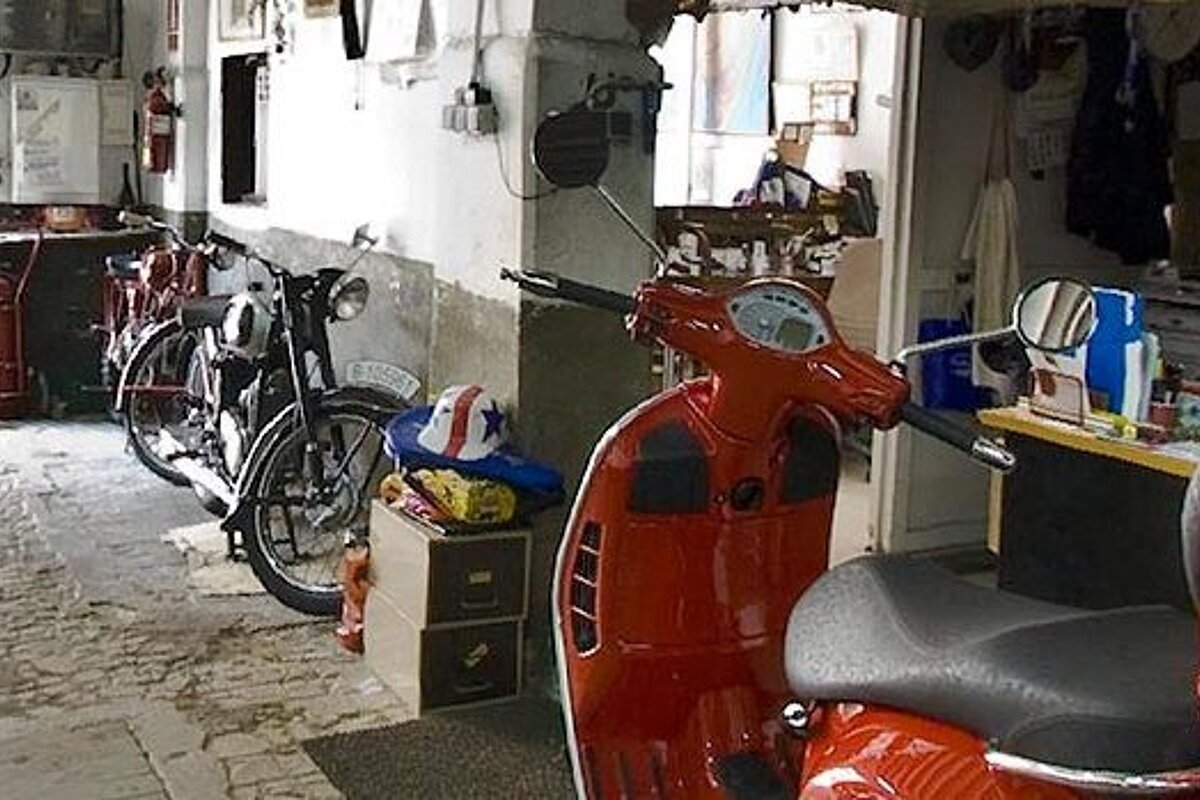 A red scooter is parked in a garage next to a motorcycle