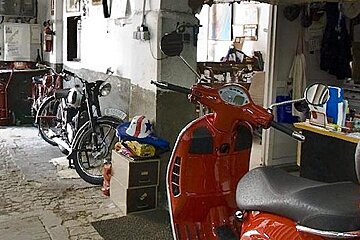 A red scooter is parked in a garage next to a motorcycle