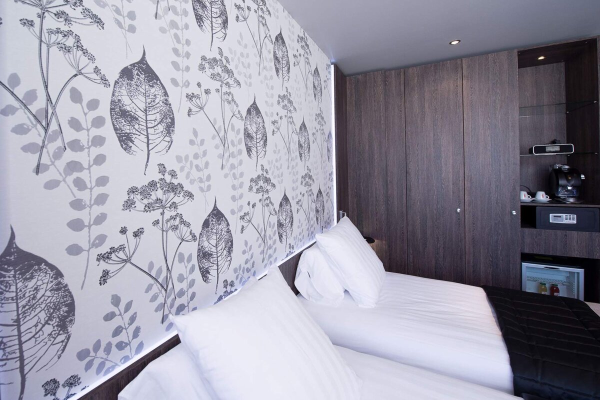 A bed in a hotel room with a floral wallpaper on the wall